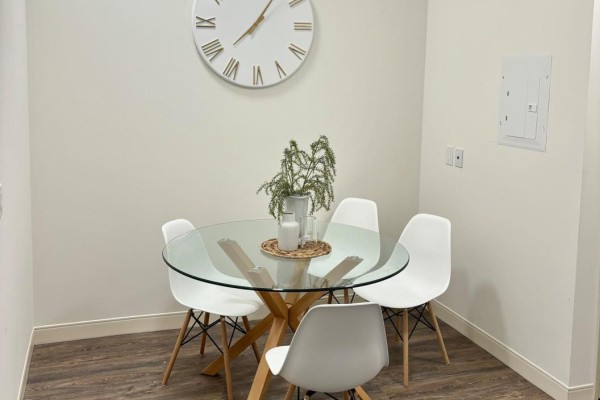 Dining area with glass-top table, four white chairs, and a large clock on the wall. - 405 - 135 Station Street, Belleville