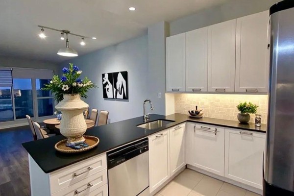 Kitchen with white cabinets, black countertops, stainless steel appliances, and dining area view. - 405 - 2470 Prince Michael Drive, Oakville