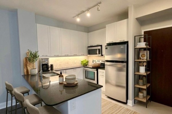 Kitchen with a breakfast bar, light grey stools, white cabinets, and stainless steel appliances. - 405 - 2470 Prince Michael Drive, Oakville