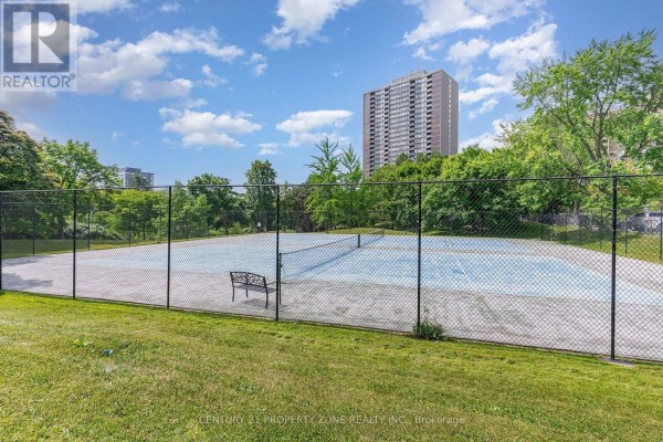 Outdoor tennis court with blue surface, chain-link fence, and a metal bench in a grassy area. - 405 - 3100 Kirwin Avenue, Mississauga