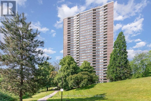 Exterior of a brick apartment building with many windows, surrounded by mature trees and green lawn. - 405 - 3100 Kirwin Avenue, Mississauga