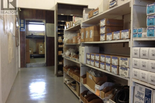 Aisle with neatly arranged boxes and plumbing supplies, leading to a back room. - 405 & 407 Railway Avenue, Weyburn