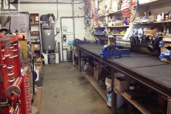 Workshop area with a large workbench, tools, and equipment for plumbing services. - 405 & 407 Railway Avenue, Weyburn