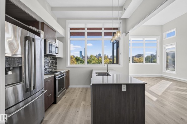 Kitchen with stainless steel appliances, island, and large windows overlooking city. - #405 10227 115 St Nw, Edmonton