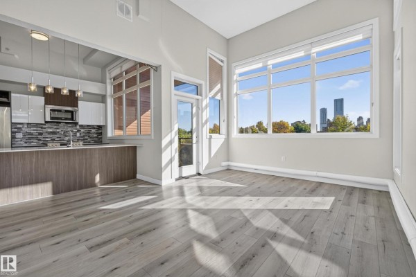 Open concept living area with kitchen, large windows, and light wood floors. - #405 10227 115 St Nw, Edmonton