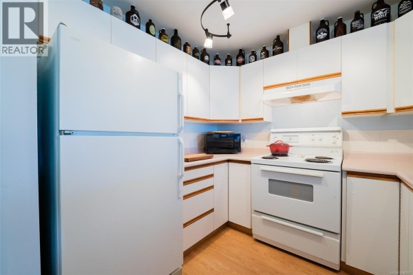 White kitchen features a stove, double sink, dishwasher, and light wood laminate flooring. - 405 1631 Dufferin Cres, Nanaimo