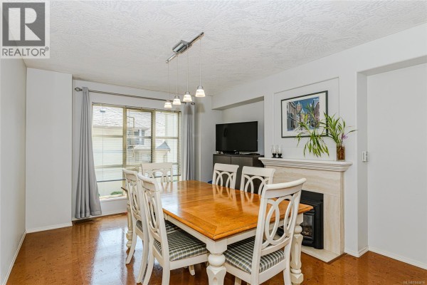 Dining area with a wooden table, white chairs, and a marble fireplace. - 405 510 Marsett Pl, Saanich