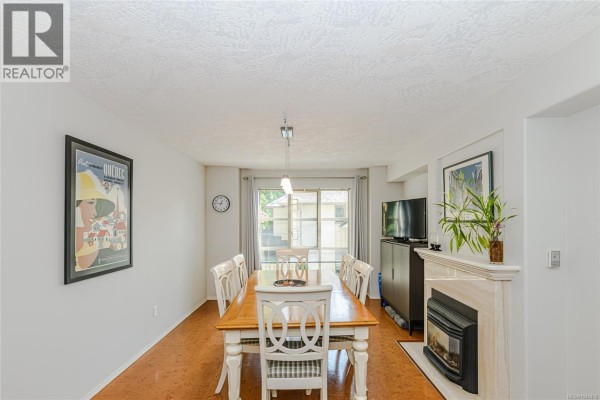 Interior view of a dining room with a table, chairs, fireplace, and large window. - 405 510 Marsett Pl, Saanich