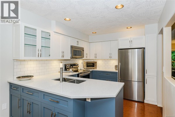 Modern kitchen with white and blue cabinets, quartz countertops, and stainless steel appliances. - 405 510 Marsett Pl, Saanich