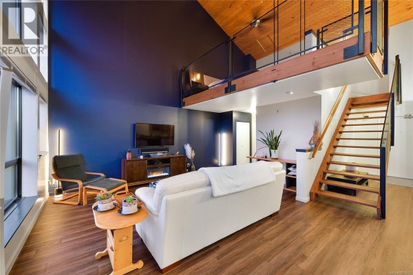 Living area with loft, wooden staircase, white sofa, and view of the dining area. - 405 829 Goldstream Ave, Langford