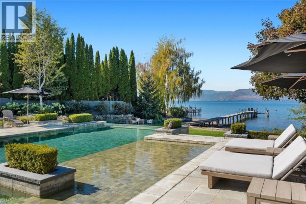 Infinity pool with lake view, lounge chairs, and a wooden dock stretching into the water. - 405 Hobson Crescent, Kelowna