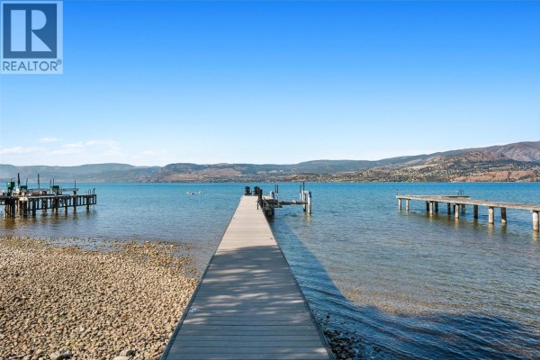 Long wooden pier extending into the lake with distant mountains and clear blue sky. - 405 Hobson Crescent, Kelowna