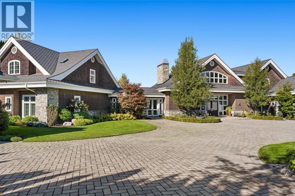 Grand entrance to a stone and wood-clad residence with a circular paver driveway and green lawn. - 405 Hobson Crescent, Kelowna