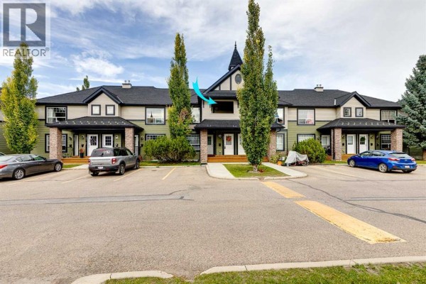 Front exterior of a green townhouse complex with multiple units and parked cars. - 406, 140 Sagewood Boulevard Sw, Airdrie