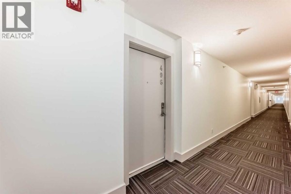 Interior hallway with white walls, modern light fixtures, and a carpeted floor with geometric pattern. - 406, 4303 1 Street Ne, Calgary