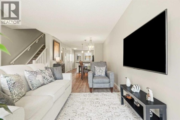 Living room with a white sofa, grey armchair, TV on wall, and view to dining area. - 406, 50 Westland Road, Okotoks