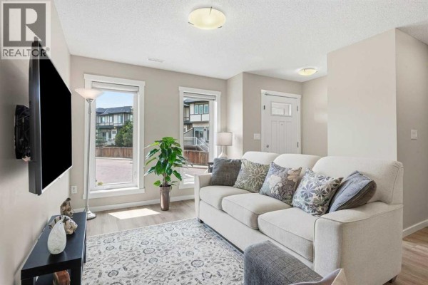 Living room with windows overlooking neighboring townhouses and green landscaping. - 406, 50 Westland Road, Okotoks