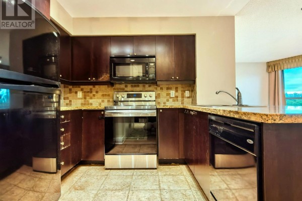 Compact kitchen with dark wood cabinets, granite countertops, stainless steel appliances, and beige tiled backsplash. - 406 - 15 Greenview Avenue, Toronto