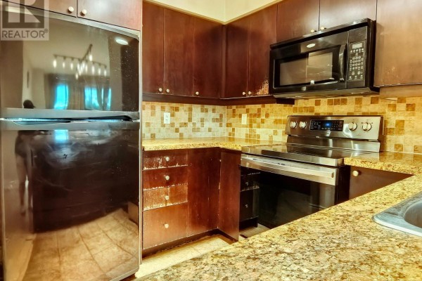 Corner view of a kitchen showing dark wood cabinets, granite countertops, and stainless steel appliances. - 406 - 15 Greenview Avenue, Toronto