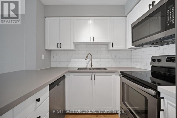 Modern white kitchen with gray countertops, stainless steel appliances, and subway tile backsplash. - 406 - 18 Stafford Street, Toronto