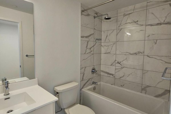 Bathroom with a white vanity, toilet, and a bathtub surrounded by marble-patterned tile. - 406 - 181 Sheppard Avenue E, Toronto