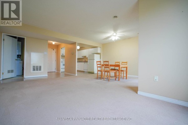 Apartment living and dining area with carpet, a small table, and an open kitchen view. - 406 - 30 Chapman Court, London North