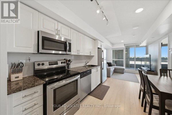 Kitchen with white cabinets, stainless steel appliances, granite counters, and open living area. - 406 - 3091 Dufferin Street, Toronto