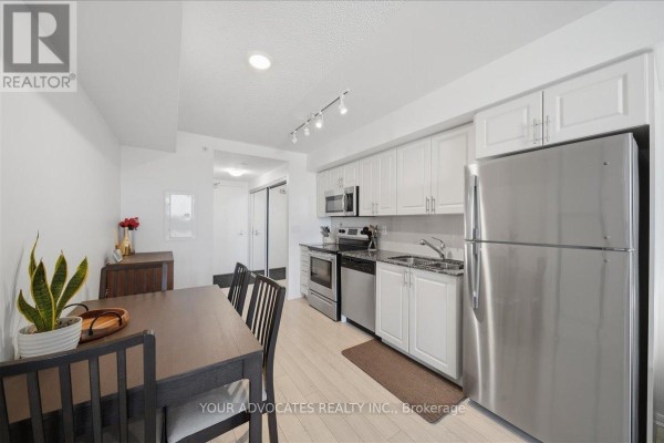 Dining area with dark wood table, chairs, and view of the kitchen and hallway. - 406 - 3091 Dufferin Street, Toronto