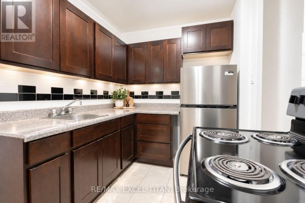 Apartment kitchen with dark wood cabinets, stainless steel refrigerator, and checkered backsplash. - 406 - 4 Hill Heights Road, Toronto