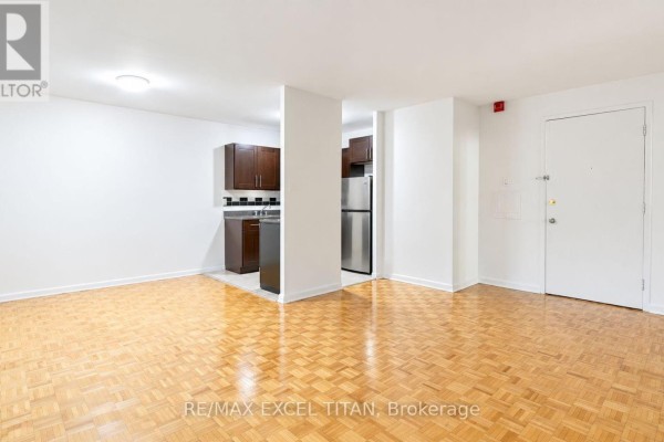 Living area with light wooden parquet flooring and view into kitchen with dark cabinets. - 406 - 4 Hill Heights Road, Toronto
