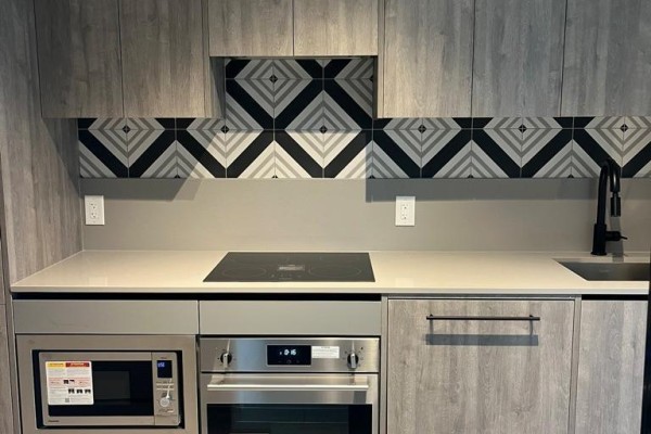Close-up of a modern kitchen with grey wood cabinets, a black backsplash, and stainless steel appliances. - 406 - 5 Lakeview Avenue, Toronto