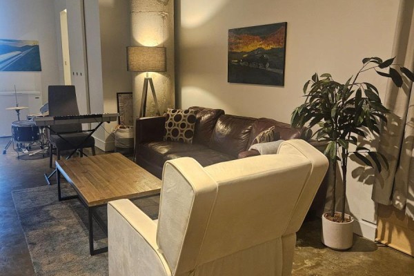 Cozy living room area with leather sofa, armchair, coffee table, keyboard, and drum set. - 406 - 90 Sumach Street, Toronto