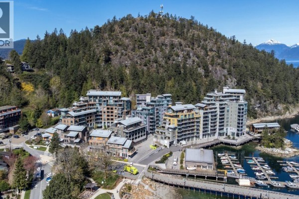View of the multi-story apartment building with balconies and glass windows next to a marina. - 406 6707 Nelson Avenue, West Vancouver