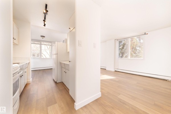 View from kitchen into a bright living area with light wood floors and white walls. - #406 9816 112 St Nw, Edmonton