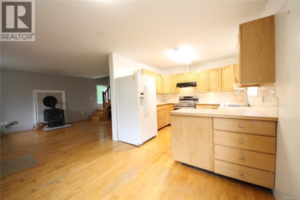 Living room with wood floors, grey walls, a wood stove, and a wooden staircase leading to the upper floor. - 406 Ferris Rd, Zeballos