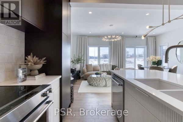 View from kitchen island to open-concept living and dining area with large windows and beige furniture. - 406 Green Gate Boulevard, Cambridge
