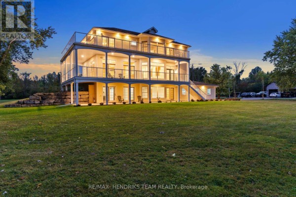 Side view of a large, light yellow house with three levels of balconies and a lower-level patio. - 4069 Niagara River Parkway, Fort Erie
