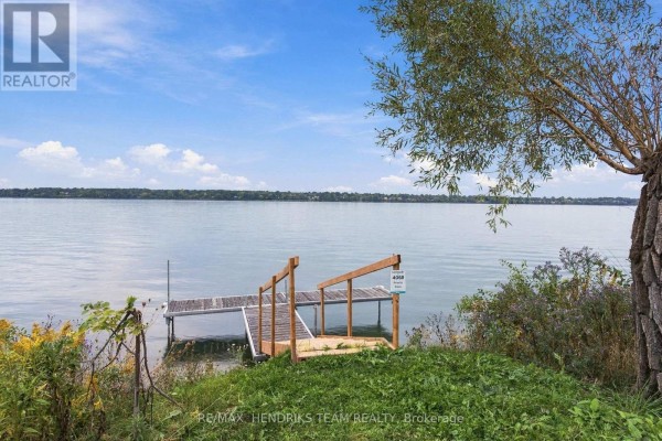 A wooden dock with a staircase leads to the calm, wide water of a lake under a blue sky. - 4069 Niagara River Parkway, Fort Erie