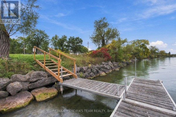 A wooden dock with a staircase is nestled between large rocks along the edge of a clear body of water. - 4069 Niagara River Parkway, Fort Erie