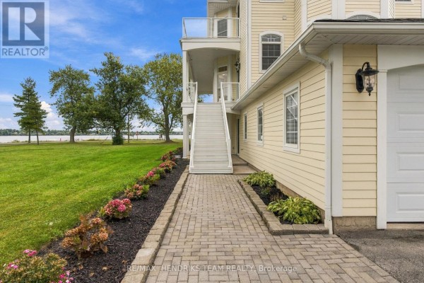 A paved walkway with landscaped flower beds leads to the side entrance and attached garage of a yellow house. - 4069 Niagara River Parkway, Fort Erie