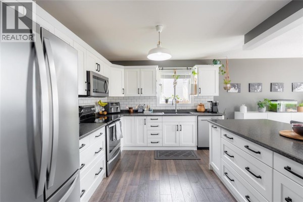 Modern kitchen with white cabinets, stainless steel appliances, dark countertops, and a large island. - 4069 Pine Crescent, Petrolia