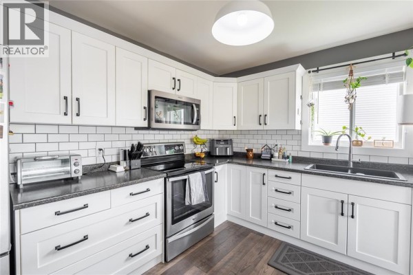 Kitchen view showing white cabinets, subway tile backsplash, stainless steel oven and microwave, and a sink. - 4069 Pine Crescent, Petrolia