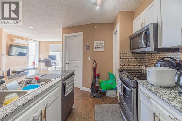 Kitchen view with granite island, white cabinets, stainless steel appliances, and open doorway. - 407, 10 Kincora Glen Park Nw, Calgary