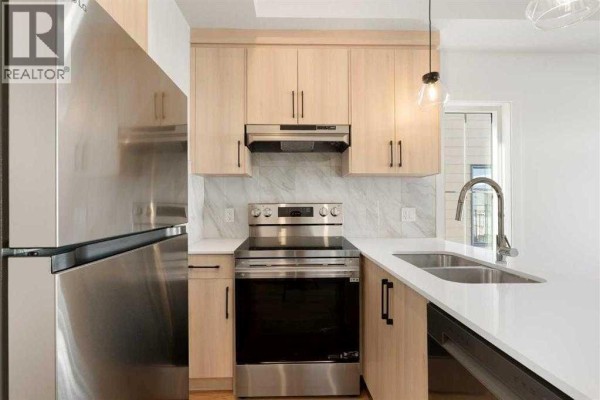 Kitchen with light wood cabinets, stainless steel appliances, and a white island with a sink. - 407, 156 Park Street, Cochrane