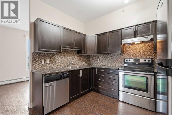 Kitchen area with dark wood cabinets, stainless steel appliances, and a view into the living space. - 407, 4901 46 Street, Red Deer