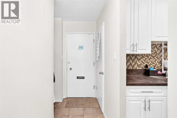 Interior view of a hallway with a white door, tiled floor, and white cabinets. - 407, 903 19 Avenue Sw, Calgary