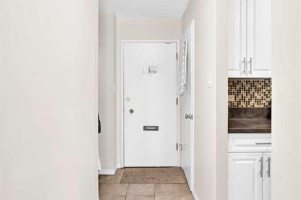 Interior view of a hallway with a white door, tiled floor, and white cabinets. - 407, 903 19 Avenue Sw, Calgary