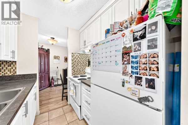Kitchen area with white cabinets, a white stove, a tiled backsplash, and a refrigerator covered in photos. - 407, 903 19 Avenue Sw, Calgary