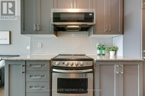 Close-up of stainless steel stove, microwave, grey cabinets, and granite countertop with subway tile backsplash. - 407 - 50 Lynn Williams Street, Toronto