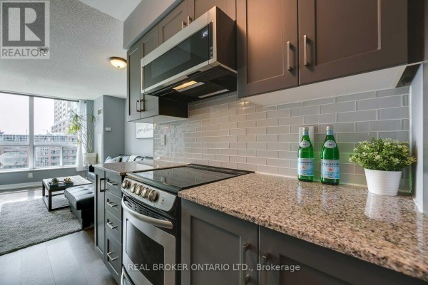View of the kitchen showing grey cabinets, stainless steel stove, granite countertops, and subway tile backsplash. - 407 - 50 Lynn Williams Street, Toronto